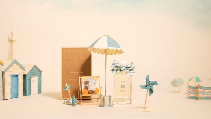 A stop motion video shows a seaside scene with a seagull on a deckchair next to a cologne and blue and white beach accessories. 